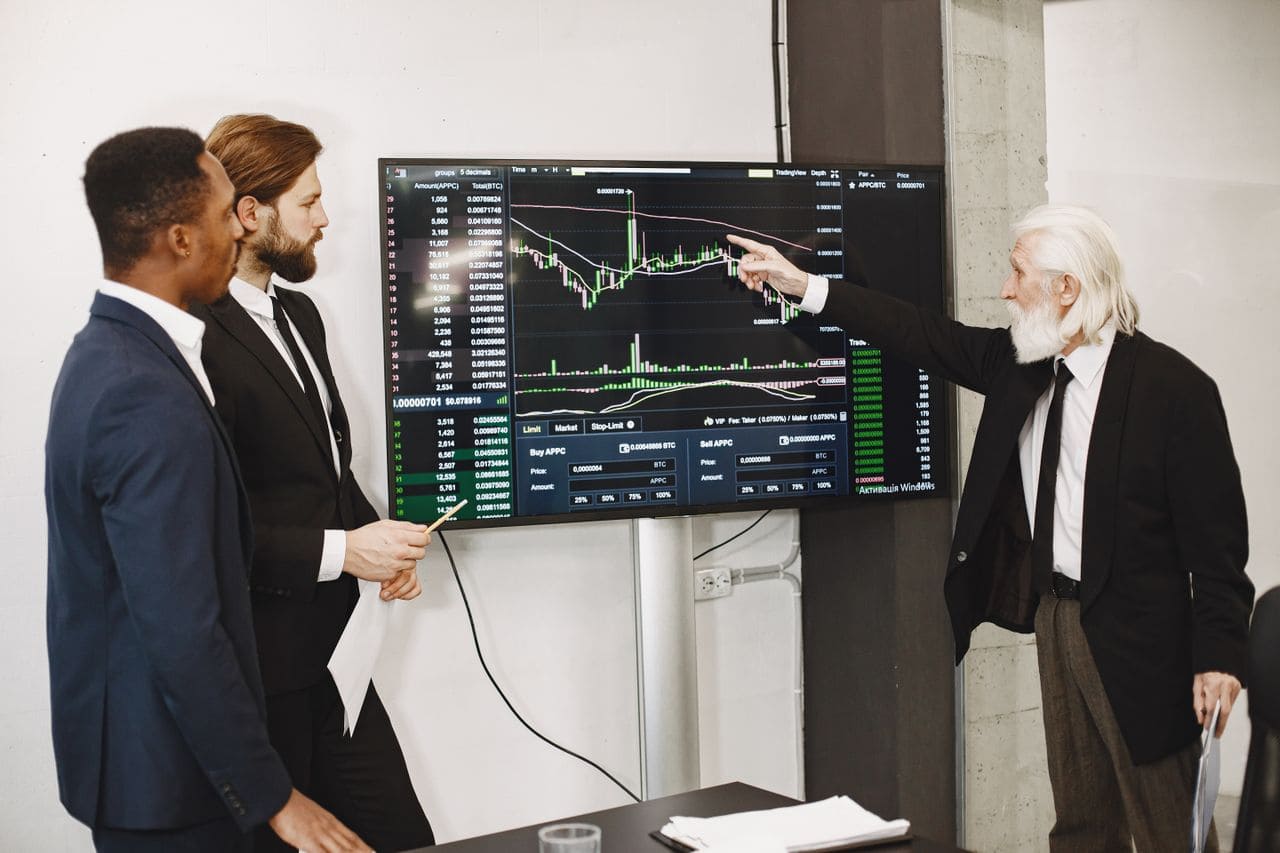Três executivos em reunião corporativa analisando gráficos financeiros e dados de engenharia de custos para redução inteligente de despesas