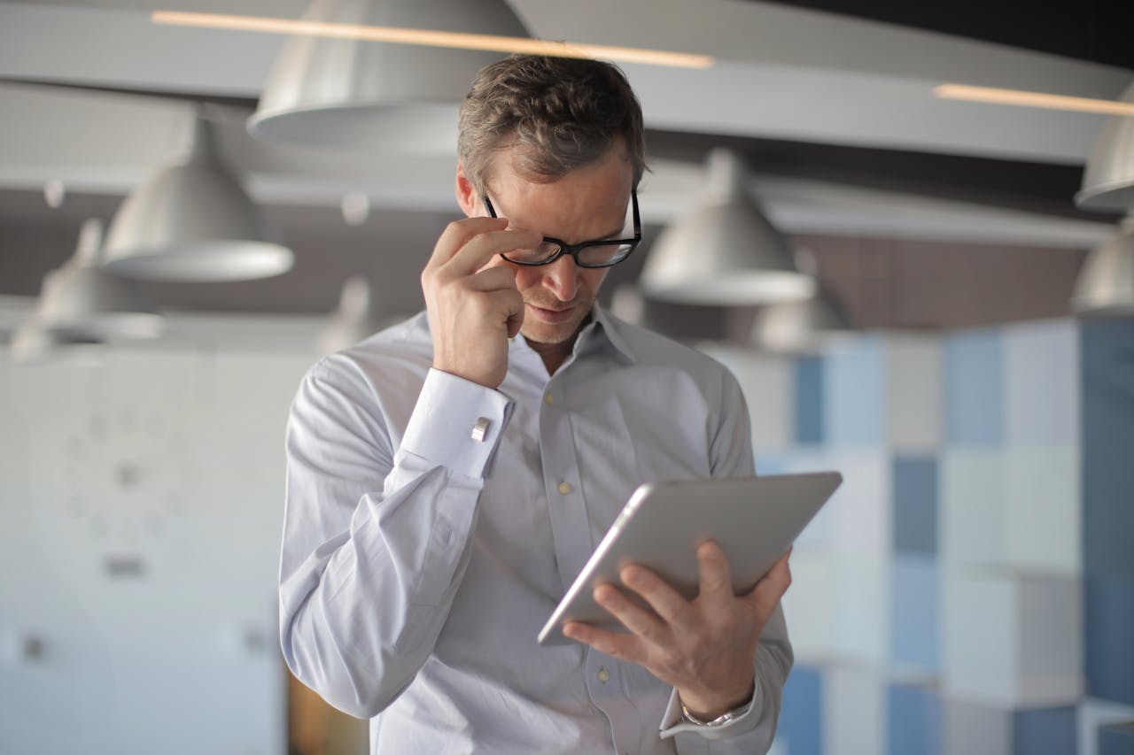 Executivo com expressão séria analisa dados financeiros em um tablet dentro de um escritório corporativo moderno.