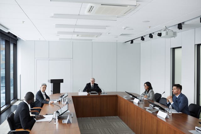 Reunião de Conselho de Gestão com executivos e conselheiros independentes debatendo estratégias ao redor de uma mesa de conferência.