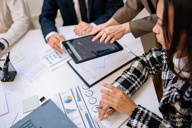 Close nas mãos de executivos em reunião estratégica analisando gráficos financeiros e relatórios em um tablet sobre a mesa.